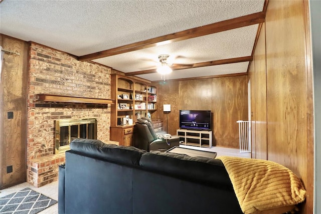 carpeted living room featuring wood walls, ceiling fan, a fireplace, a textured ceiling, and beamed ceiling