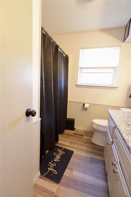 bathroom with hardwood / wood-style floors, vanity, a textured ceiling, and toilet