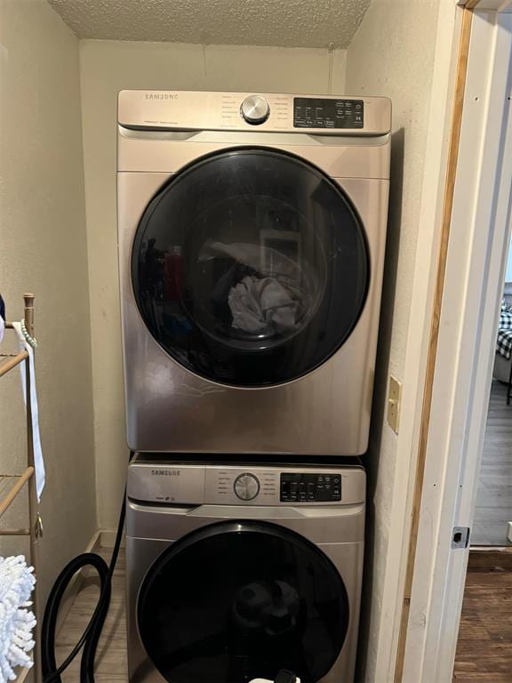 laundry room with wood-type flooring, stacked washing maching and dryer, and a textured ceiling