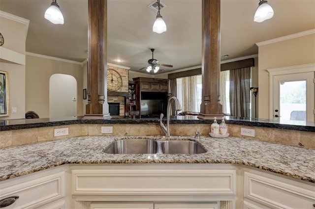 kitchen with ceiling fan, sink, light stone countertops, decorative light fixtures, and ornamental molding