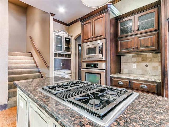 kitchen with stainless steel appliances, backsplash, dark stone countertops, light hardwood / wood-style floors, and ornamental molding