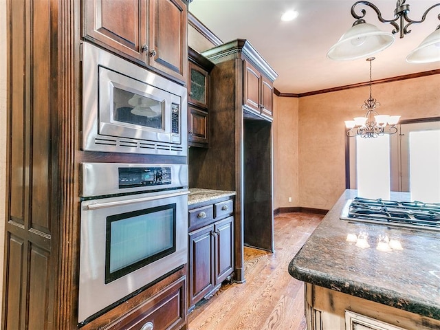 kitchen featuring dark stone countertops, dark brown cabinets, ornamental molding, and appliances with stainless steel finishes