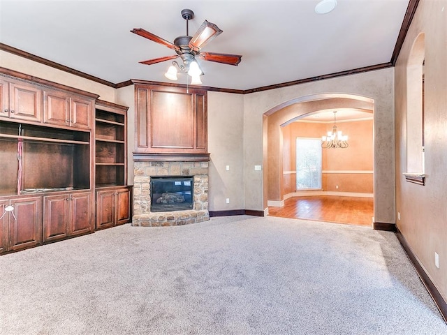 unfurnished living room featuring ceiling fan with notable chandelier, carpet floors, a stone fireplace, and crown molding