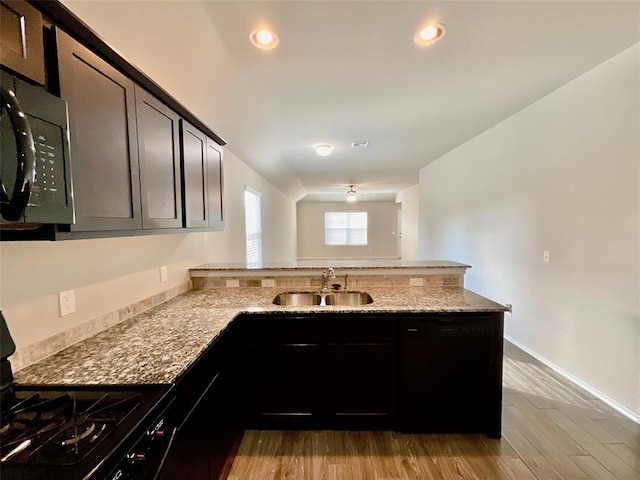 kitchen with light stone countertops, kitchen peninsula, black appliances, sink, and light hardwood / wood-style floors