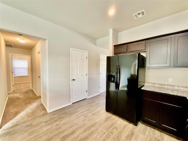 kitchen featuring dark brown cabinetry, black fridge, light stone countertops, and light wood-type flooring