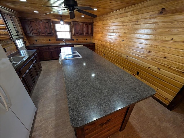 kitchen with ceiling fan, sink, wooden ceiling, a center island, and wood walls