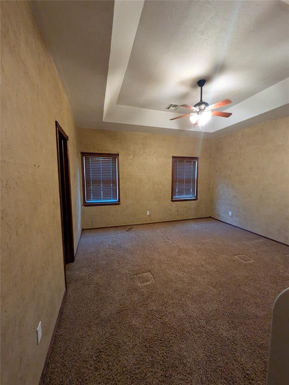 carpeted spare room featuring a raised ceiling and ceiling fan