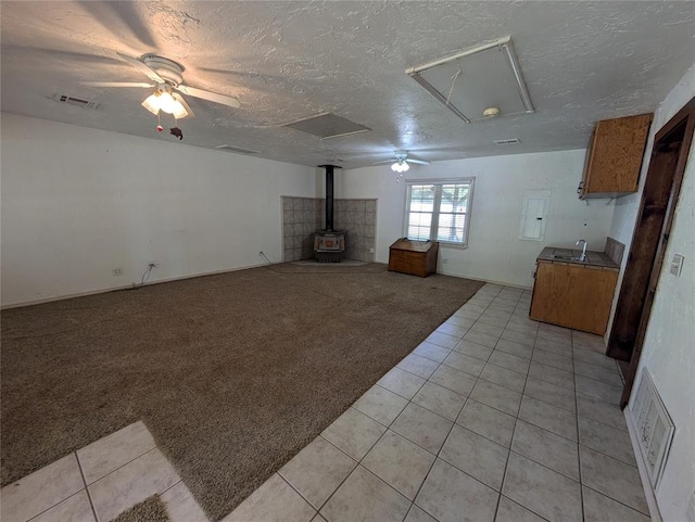 unfurnished living room with a wood stove, ceiling fan, sink, a textured ceiling, and light carpet