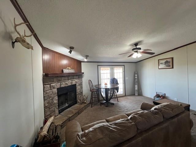 carpeted living room with a stone fireplace, crown molding, ceiling fan, and a textured ceiling