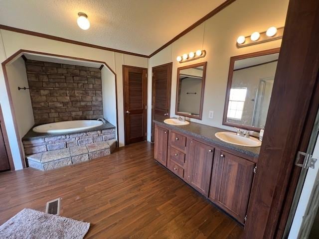 bathroom with tiled tub, wood-type flooring, a textured ceiling, lofted ceiling, and vanity