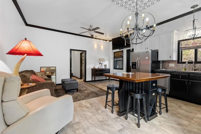 kitchen with sink, a kitchen breakfast bar, stainless steel refrigerator with ice dispenser, ceiling fan with notable chandelier, and light wood-type flooring