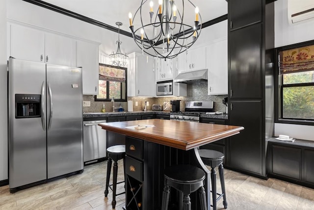 kitchen with backsplash, ornamental molding, stainless steel appliances, a center island, and hanging light fixtures