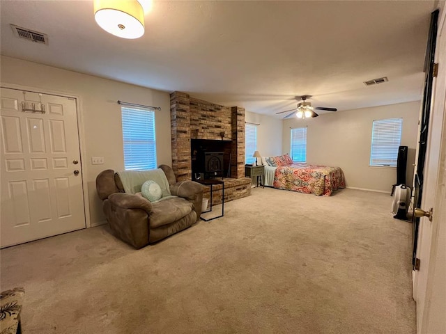 bedroom with a wood stove, ceiling fan, carpet, and multiple windows