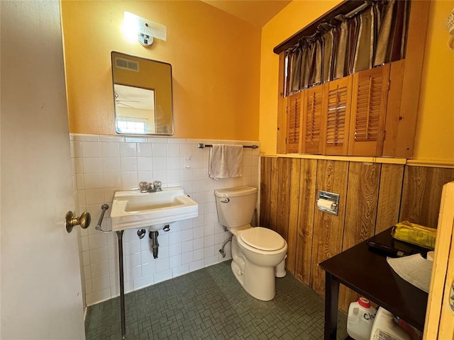 bathroom with toilet, tile patterned floors, tile walls, and sink