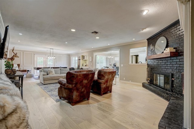 living room with a fireplace, ornamental molding, a textured ceiling, and light wood-type flooring