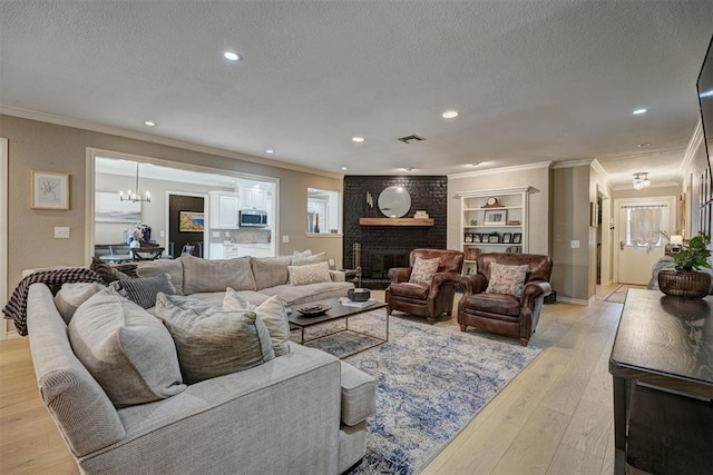 living room with a notable chandelier, light wood-type flooring, a textured ceiling, a fireplace, and ornamental molding