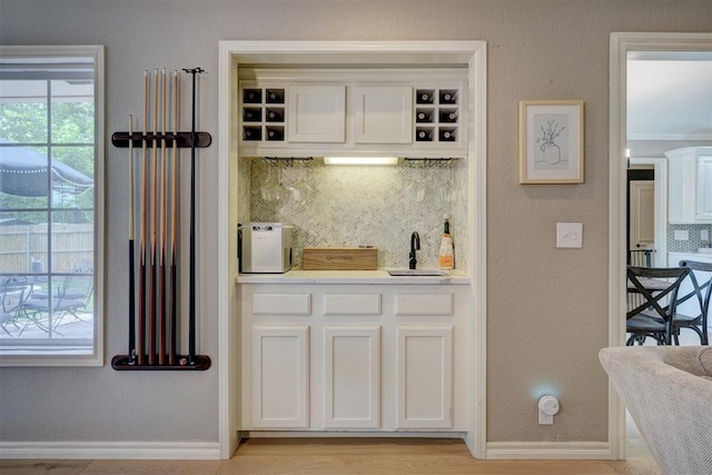 bar with decorative backsplash, white cabinetry, crown molding, and sink