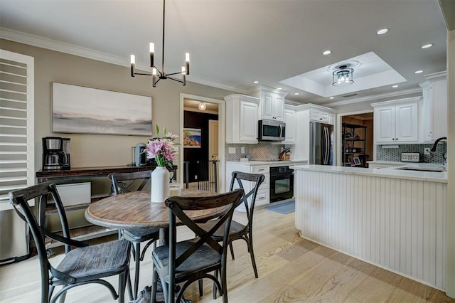 dining room featuring ornamental molding, a tray ceiling, sink, light hardwood / wood-style flooring, and an inviting chandelier