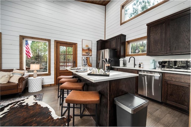 kitchen with stainless steel appliances, high vaulted ceiling, wood walls, a breakfast bar area, and a center island with sink