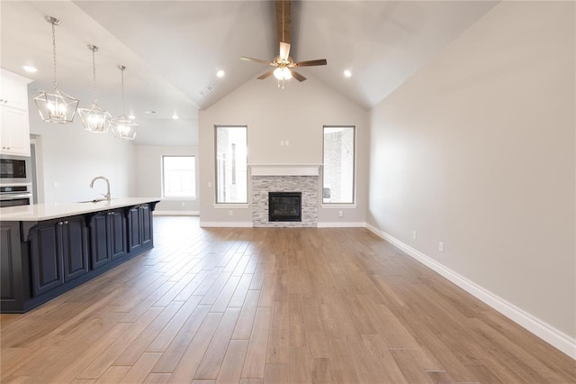 16025 Coneflower Dr, Edmond, OK 73013 - unfurnished living room featuring a sink, light wood-style floors, ceiling fan, a fireplace, and baseboards