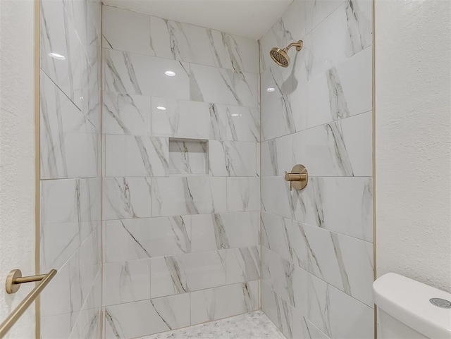 bathroom with a tile shower and toilet