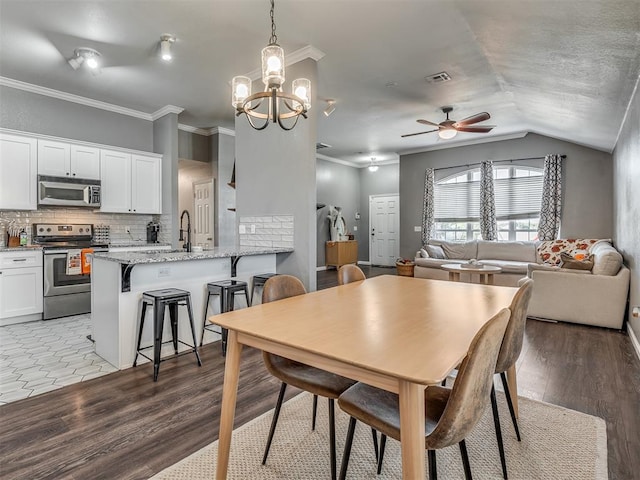 dining space featuring sink, light hardwood / wood-style flooring, ornamental molding, and vaulted ceiling