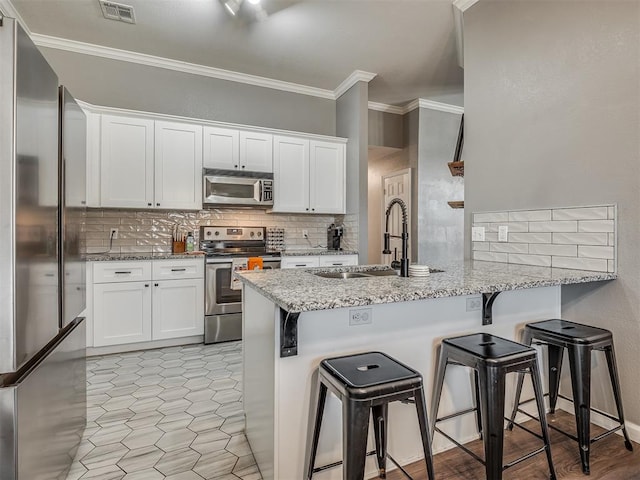 kitchen with light stone countertops, appliances with stainless steel finishes, white cabinetry, sink, and kitchen peninsula