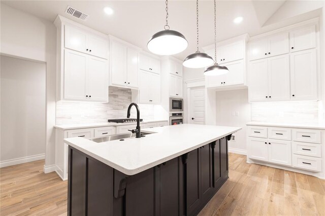 9201 Lupine Rd, Yukon, OK 73099 - kitchen featuring appliances with stainless steel finishes, baseboards, backsplash, light wood-style flooring, and a center island with sink