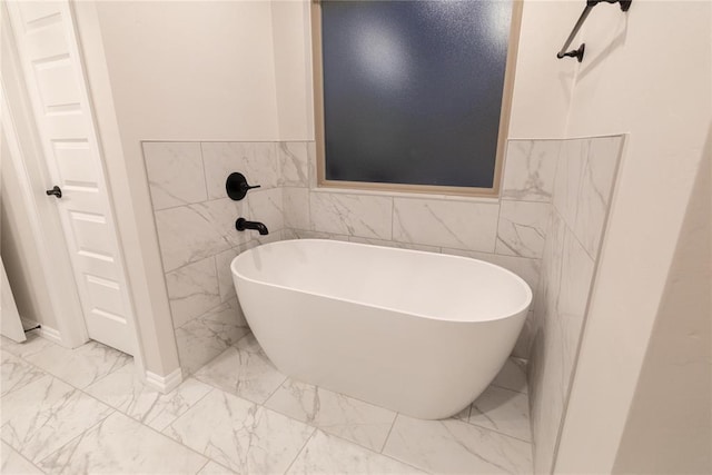 9201 Lupine Rd, Yukon, OK 73099 - bathroom featuring marble look tile flooring, tile walls, a freestanding tub, and a wainscoted wall