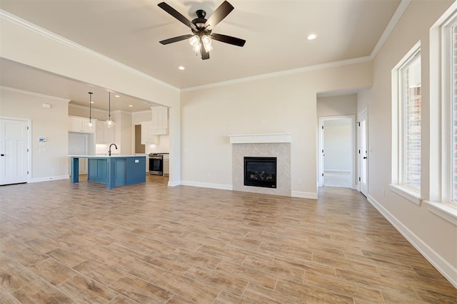 unfurnished living room with crown molding, ceiling fan, sink, and light wood-type flooring