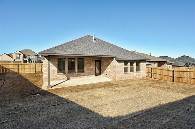 rear view of house with brick siding, roof with shingles, a patio area, and a fenced backyard