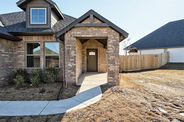 doorway to property with roof with shingles, fence, and brick siding