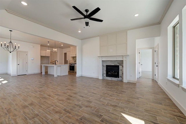 unfurnished living room featuring light wood finished floors, ornamental molding, a brick fireplace, baseboards, and ceiling fan with notable chandelier