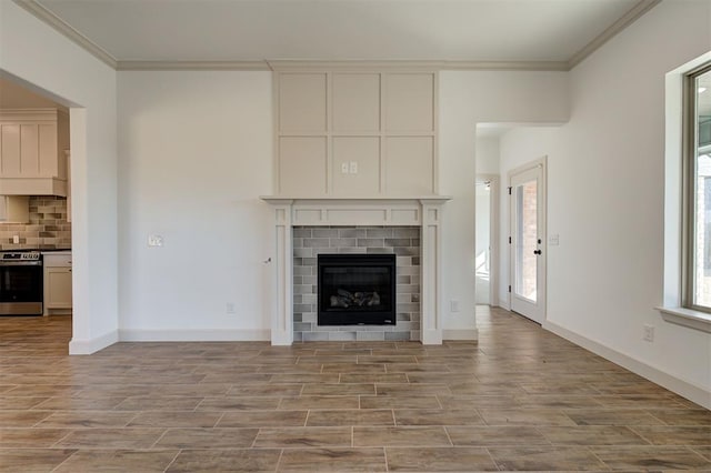 unfurnished living room with a brick fireplace, baseboards, crown molding, and wood finish floors