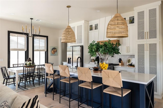 kitchen featuring stainless steel fridge with ice dispenser, light wood-type flooring, white cabinetry, and hanging light fixtures