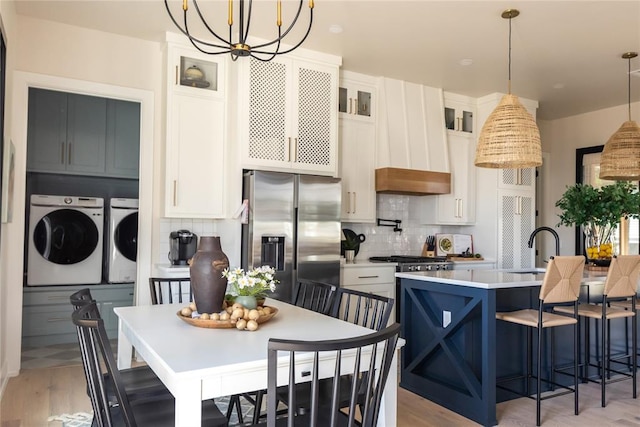 kitchen with separate washer and dryer, stainless steel fridge with ice dispenser, decorative light fixtures, a center island with sink, and white cabinets