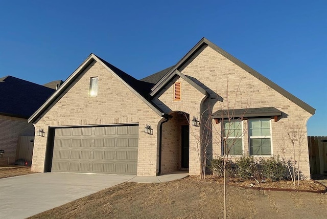 french country home with driveway, a garage, and brick siding