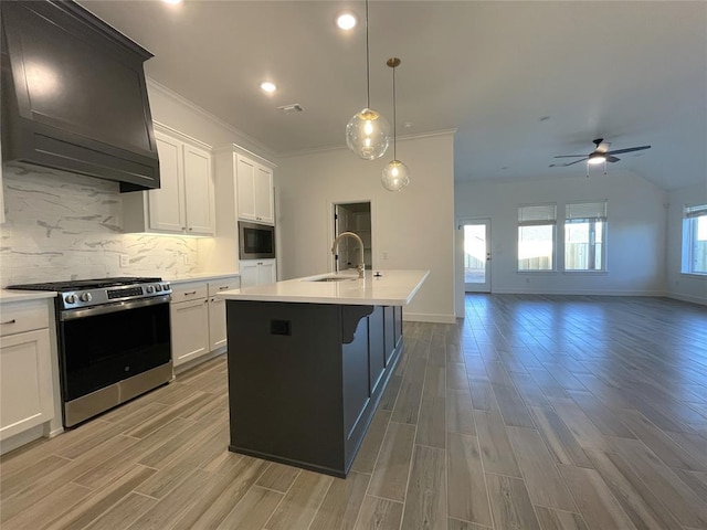 kitchen featuring a center island with sink, light countertops, custom range hood, gas stove, and a sink