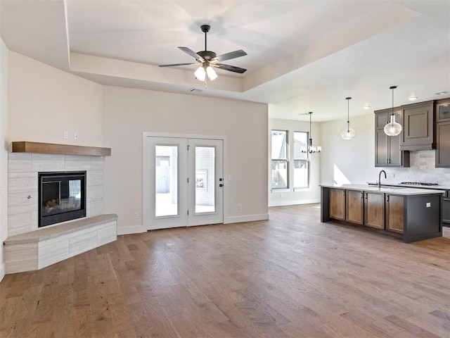 unfurnished living room featuring ceiling fan with notable chandelier, sink, hardwood / wood-style flooring, a fireplace, and a tray ceiling