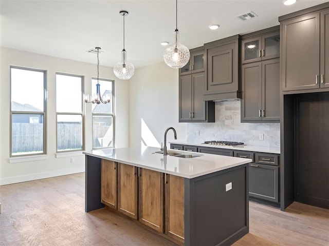 kitchen with backsplash, a kitchen island with sink, sink, pendant lighting, and light hardwood / wood-style flooring