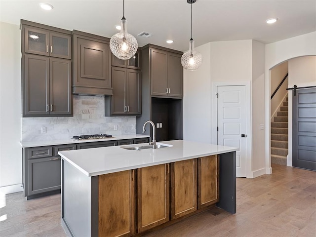 kitchen featuring decorative light fixtures, light hardwood / wood-style floors, sink, and a kitchen island with sink