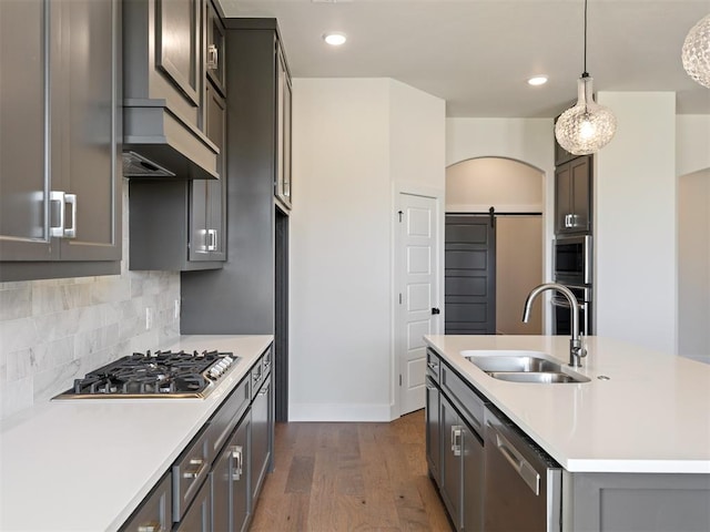 kitchen featuring dark hardwood / wood-style flooring, stainless steel appliances, sink, a barn door, and hanging light fixtures