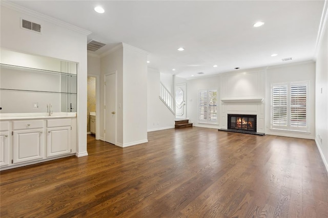 unfurnished living room with sink, a large fireplace, dark wood-type flooring, and ornamental molding