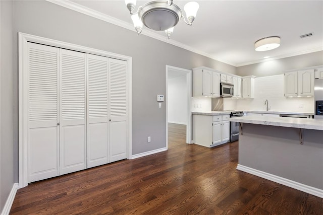 kitchen with appliances with stainless steel finishes, dark hardwood / wood-style flooring, ornamental molding, sink, and white cabinetry