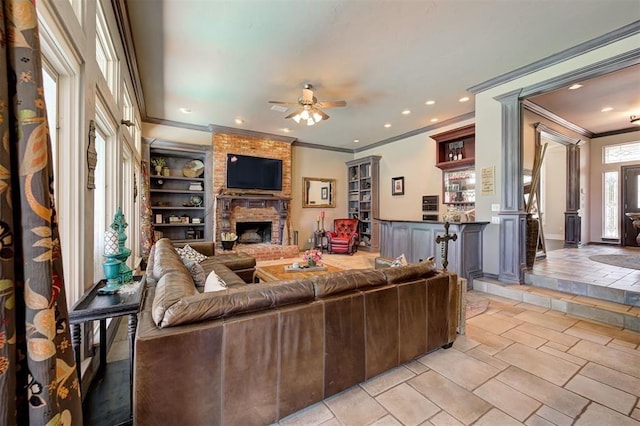 living room featuring ceiling fan, ornate columns, ornamental molding, and a brick fireplace