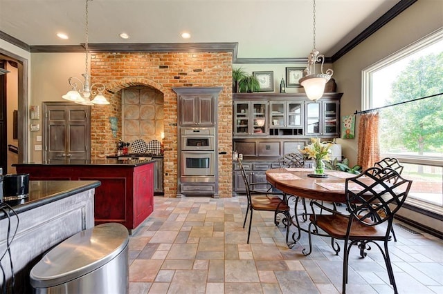 kitchen with ornamental molding, brick wall, stainless steel double oven, an inviting chandelier, and hanging light fixtures