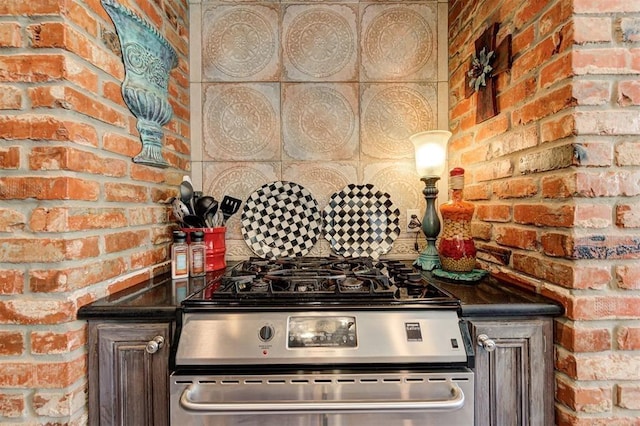 kitchen featuring dark brown cabinets, stainless steel gas stove, and brick wall