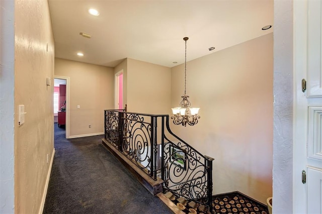 hallway featuring a chandelier and dark carpet