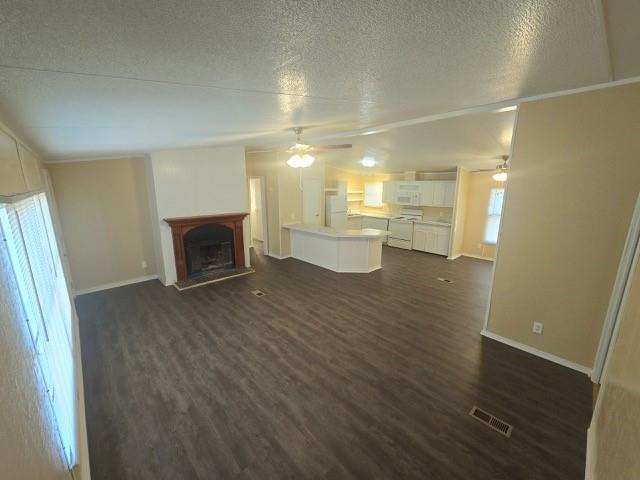 unfurnished living room with a textured ceiling, dark hardwood / wood-style flooring, and ceiling fan