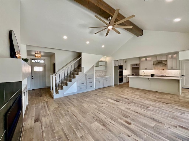 unfurnished living room with ceiling fan, beamed ceiling, high vaulted ceiling, and light wood-type flooring